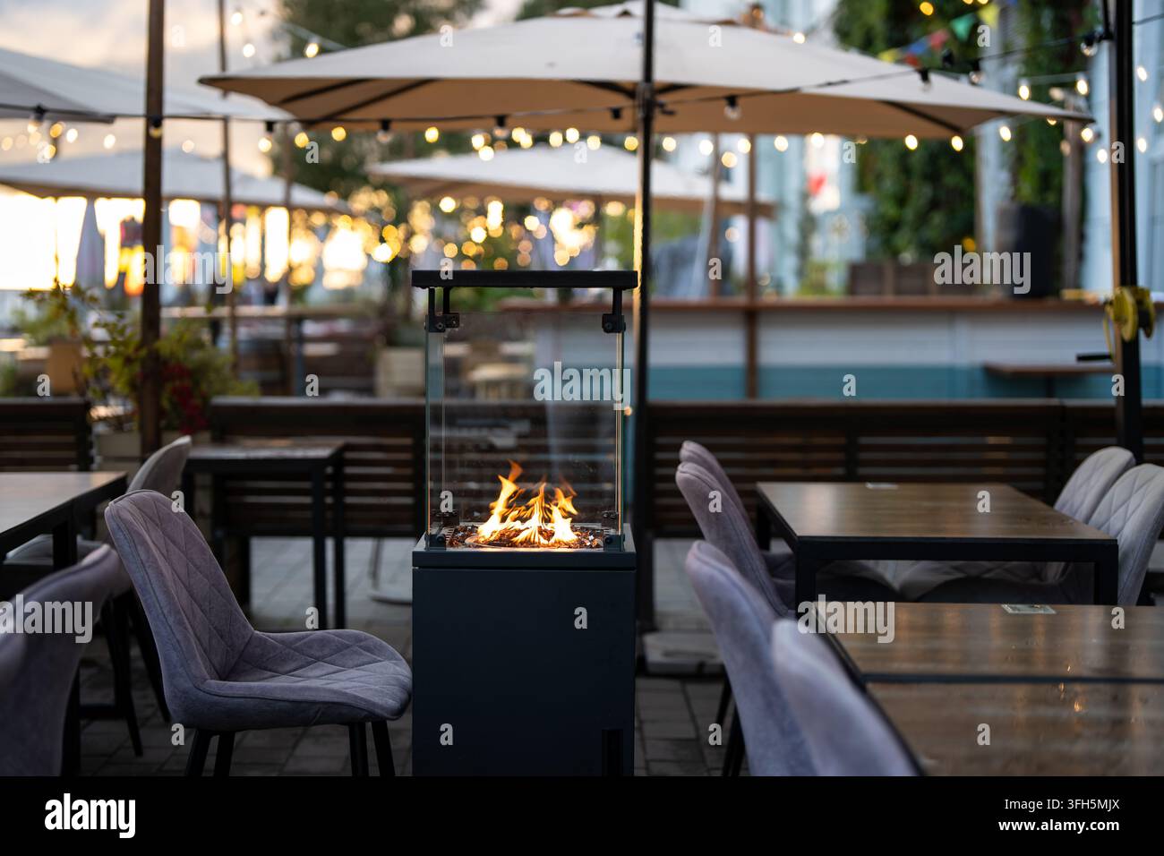 Terrasse de restaurant en plein air confortable avec canapés, parasols et cheminée à gaz moderne à l'intérieur d'une boîte en verre. Banque D'Images