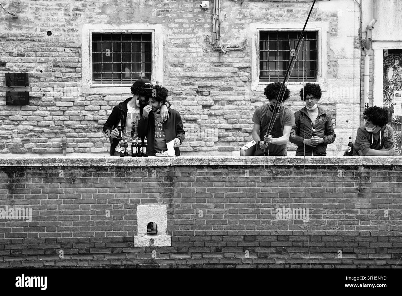 Photo en noir et blanc de jeunes hommes en perruques célébrant et pêchant le long du canal Fondamenta Toffetti à Venise, Italie Banque D'Images