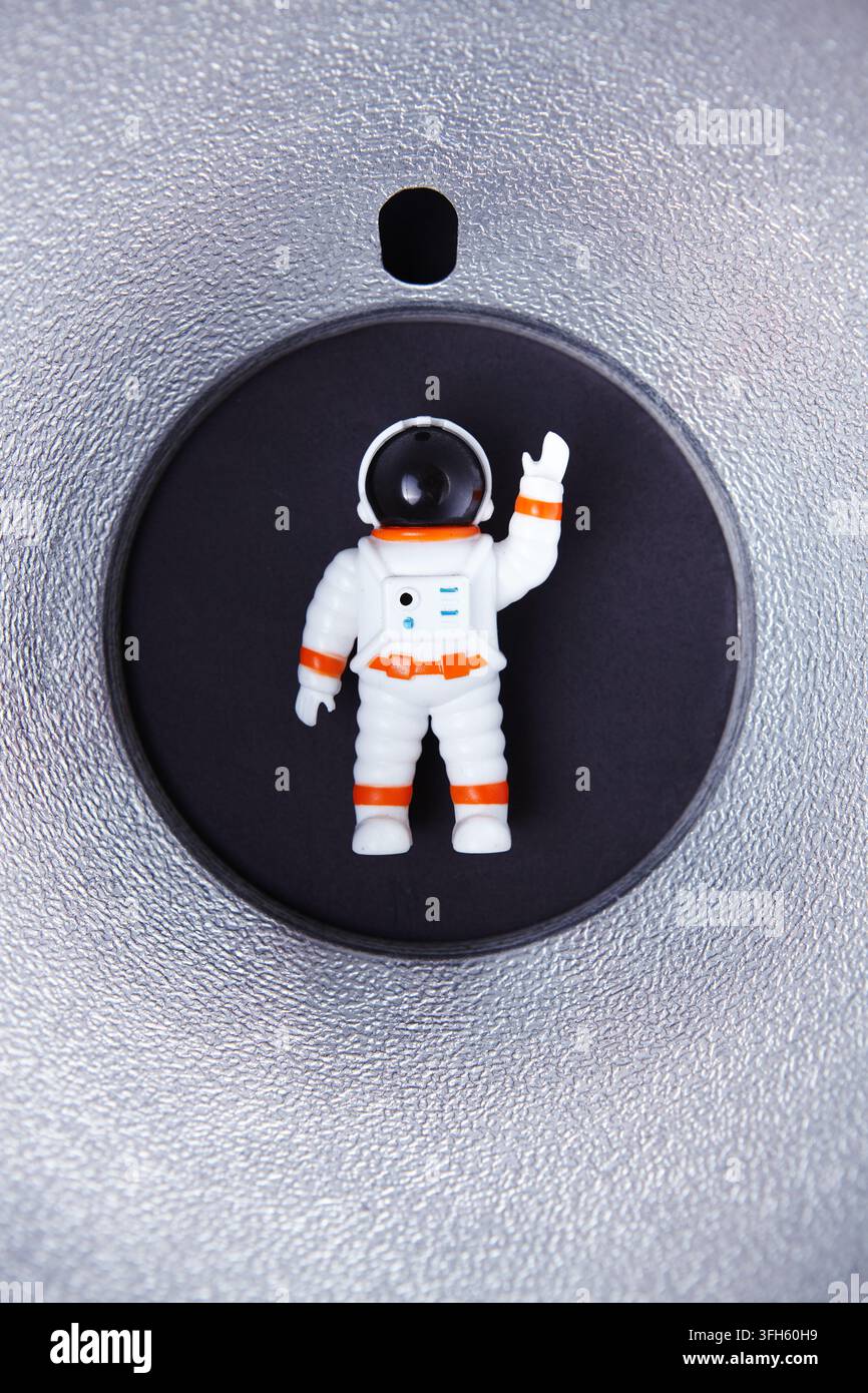Une petite figurine d'astronaute se tenant dans une zone encastrée circulaire sur un fond noir, entourée d'une finition argentée métallique. Banque D'Images