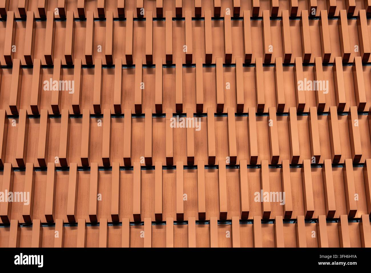gros plan d'une façade de bâtiment urbain moderne avec des lamelles verticales en bois répétitives, des tons bruns chauds, des ombres profondes et un rythme géométrique créant une abstraction Banque D'Images