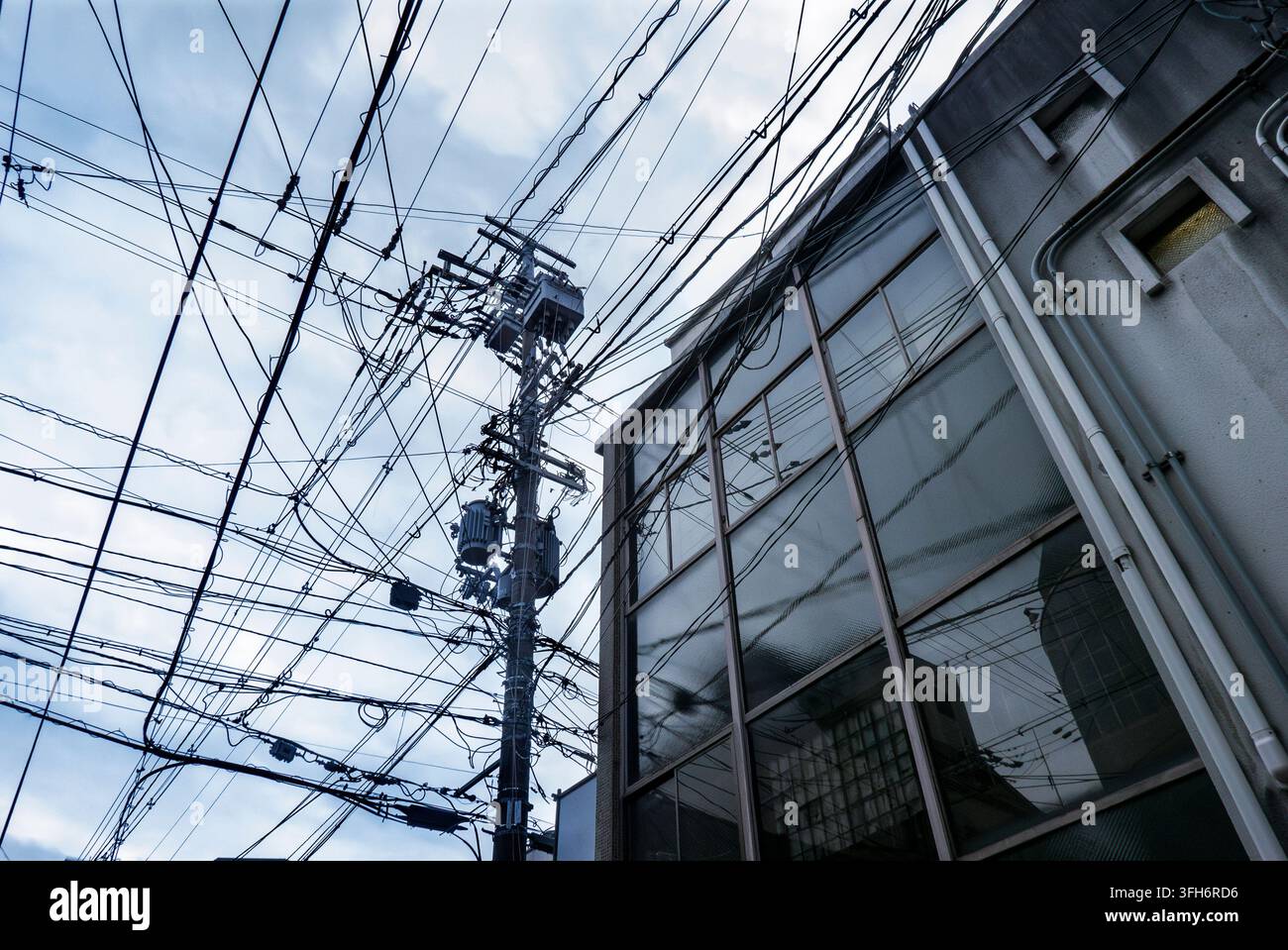 Désordre de fils électriques dans les rues de Tokyo près des fenêtres en verre d'un bâtiment. Banque D'Images