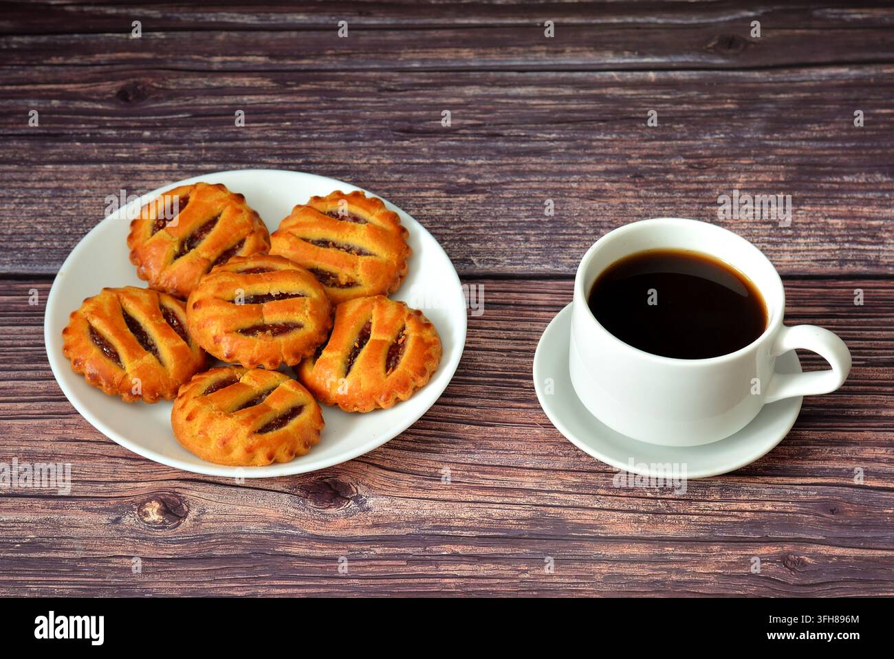 Plusieurs mini tartes à la confiture de pommes dans une assiette ronde et une tasse de café noir sur une table en bois. Vue de dessus, flat lay. Banque D'Images
