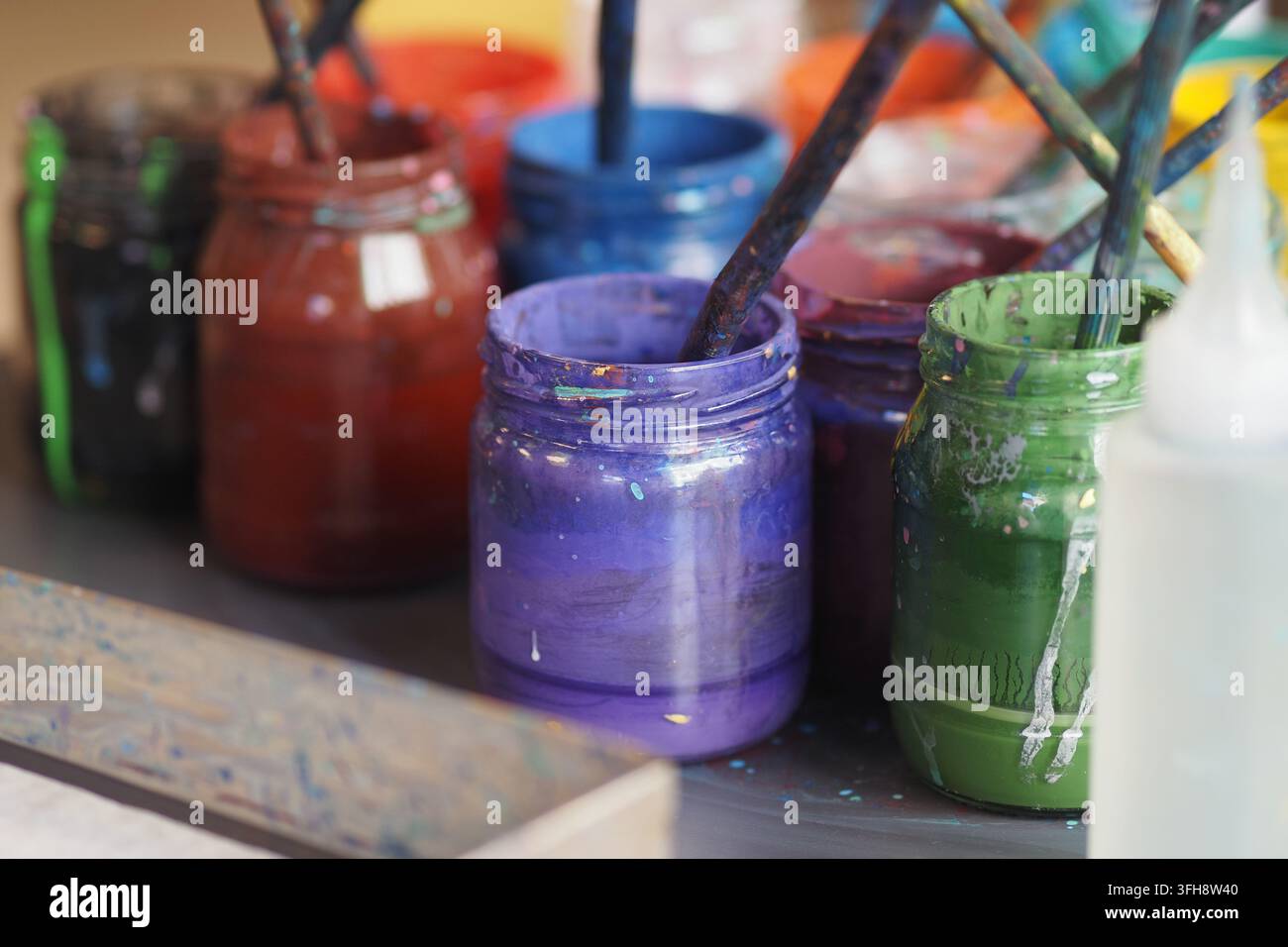 Bocaux de peinture colorés et pinceaux sur une table dans un cadre d'atelier artistique Banque D'Images