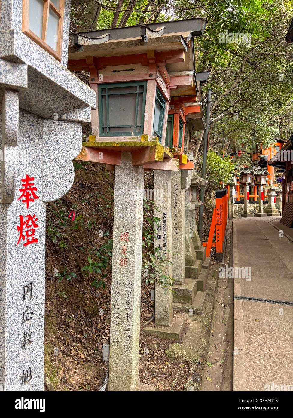 Range de lanternes en pierre de granit avec inscriptions de donateurs gravées bordant un trottoir en béton au Fushimi Inari Taisha à Kyoto, Japon. - Image de stock capturée avec un smartphone