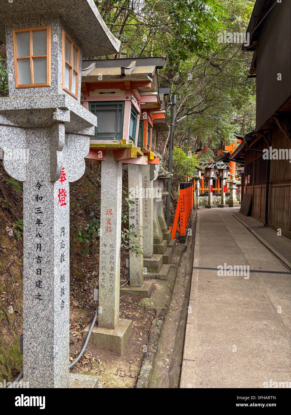 Range de lanternes en pierre de granit avec inscriptions de donateurs gravées bordant un trottoir en béton au Fushimi Inari Taisha à Kyoto, Japon. - Image de stock capturée avec un smartphone