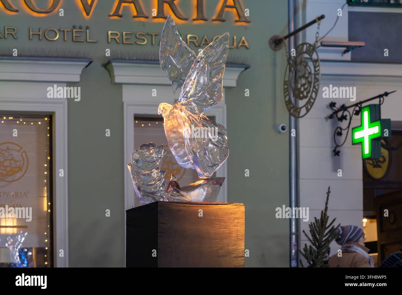 Poznań, Pologne – 13 décembre 2025 : Une sculpture sur glace illuminée d'un oiseau est posée sur un support en bois devant un hôtel de ville, évoquant l'émerveillement saisonnier dans un Banque D'Images