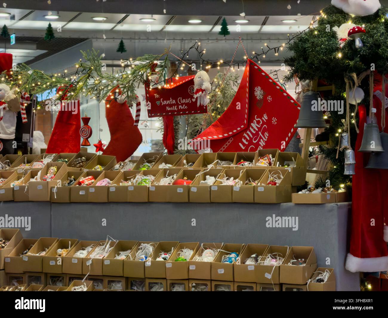 Poznań, Pologne – 13 décembre 2025 : Rangées de décorations de fêtes saisonnières disposées à la vente sur une étagère en bois près d’une boîte aux lettres du Père Noël dans un ch Banque D'Images