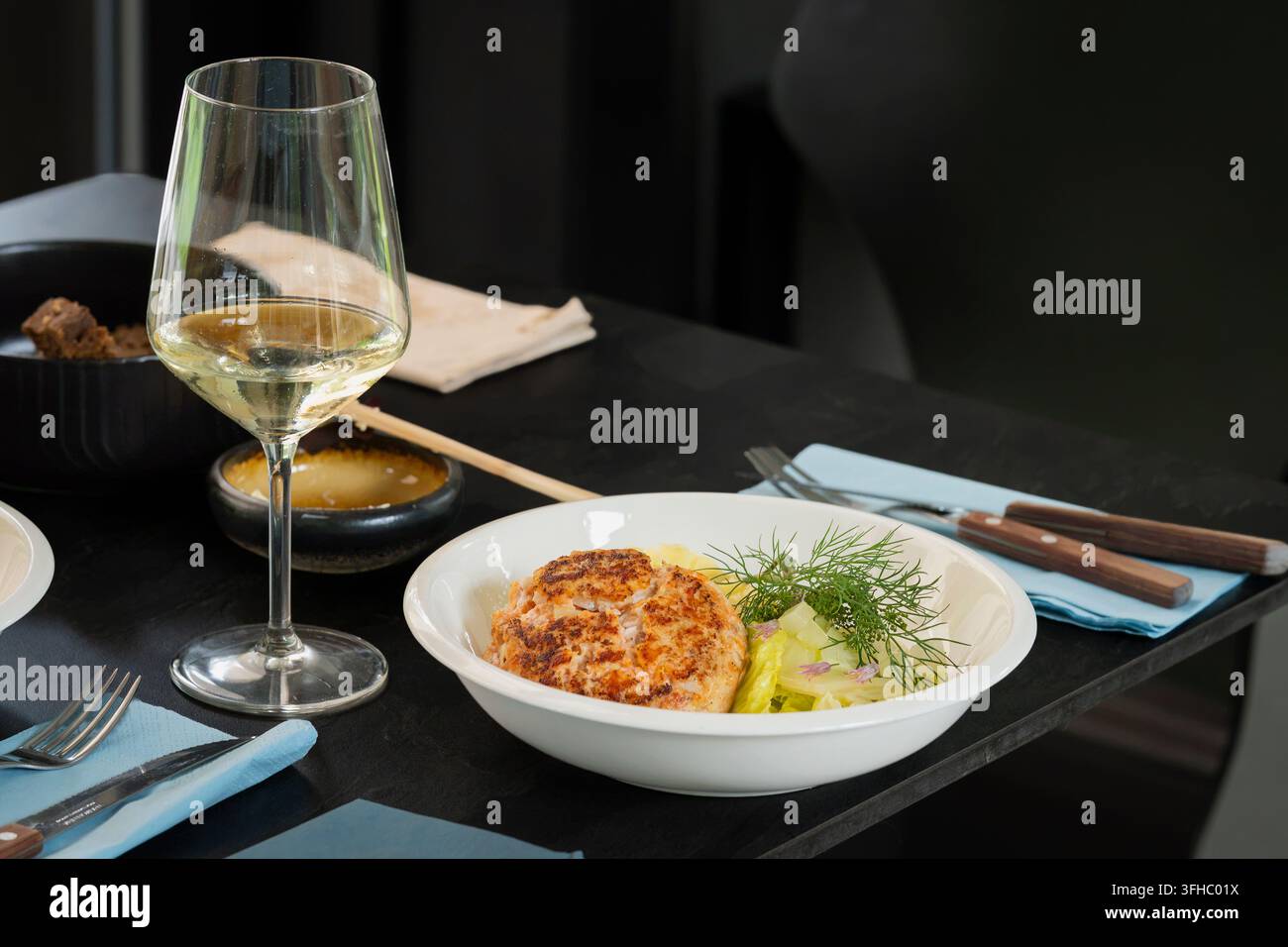 Fricassée de poisson doré servi avec une salade verte fraîche et de l'aneth aromatique, présentée dans un bol blanc sur une table à manger sombre et élégante. Banque D'Images