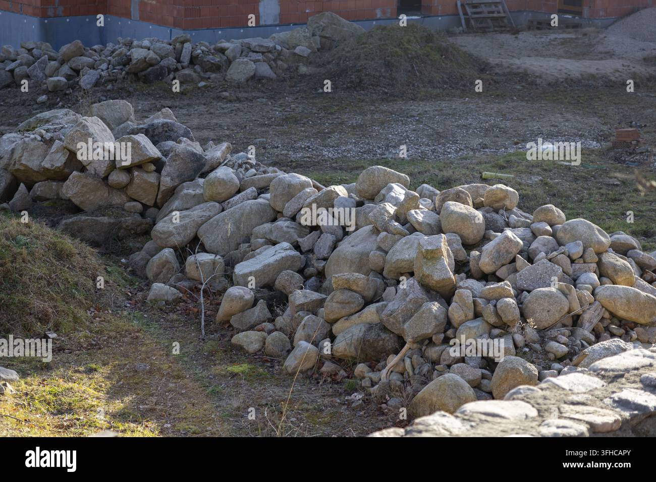 Des pierres grises naturelles abondantes sont méticuleusement empilées sur un sol herbeux d'un chantier de construction, parfaites pour la rénovation de maisons ou les projets d'aménagement paysager moderne Banque D'Images