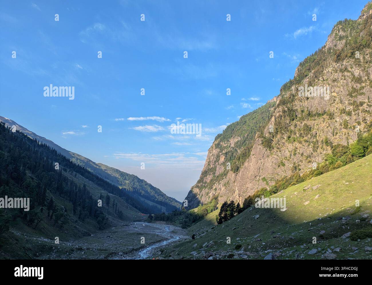 Vallée verte majestueuse et sommets montagneux escarpés sous un ciel bleu clair sur la route de randonnée du col de Hampta, Himachal Pradesh, Inde - Image de stock capturée avec un smartphone