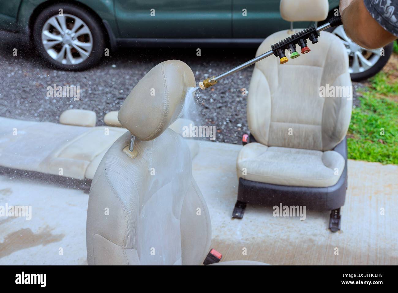 Un agent de service utilise un nettoyeur haute pression pour nettoyer les sièges de voiture à l'extérieur sur l'allée. Banque D'Images