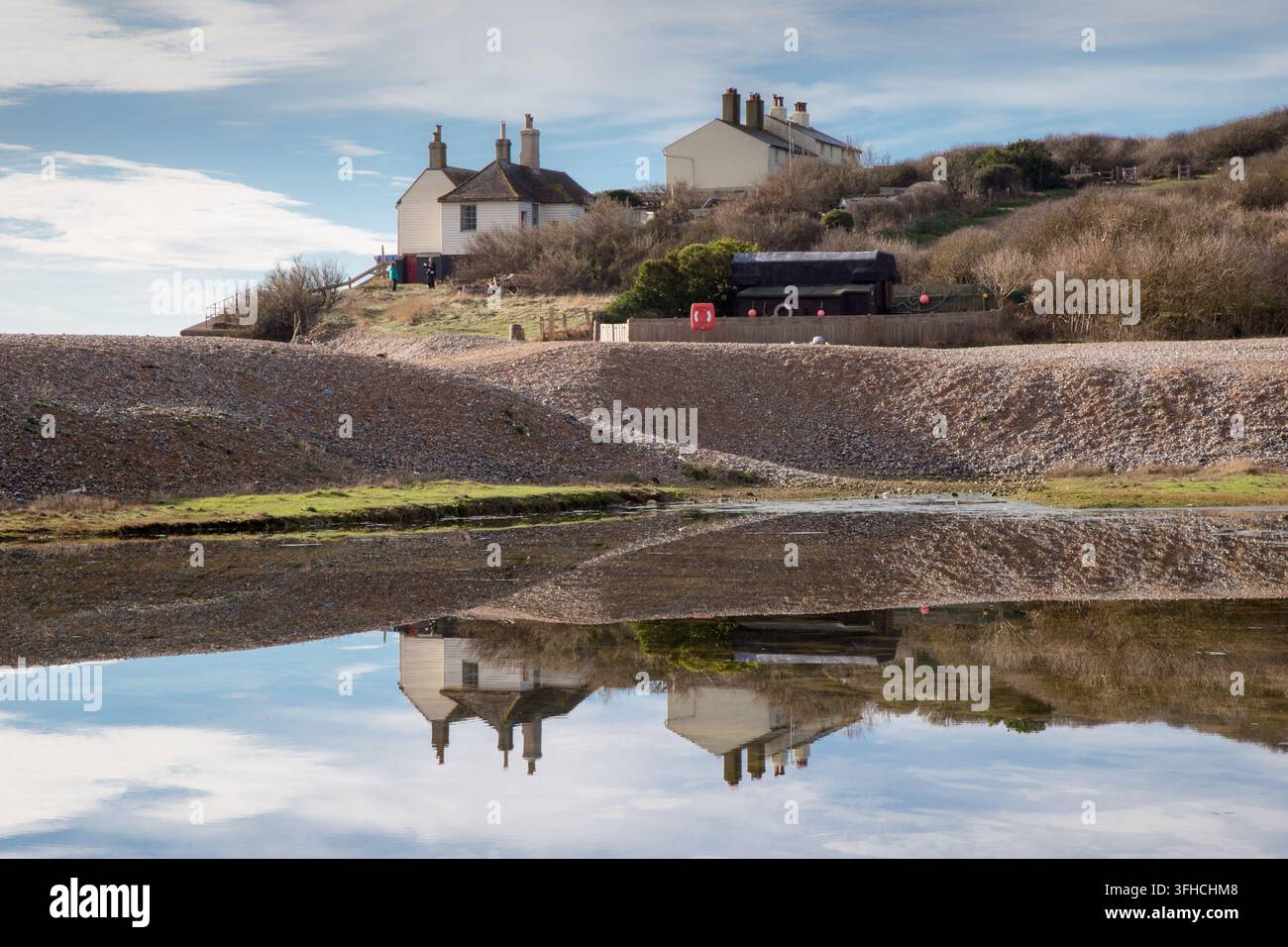 Cottages historiques des gardes-côtes parfaitement reflétés dans un plan d'eau calme derrière la plage de galets à Cuckmere Haven, East Sussex. Banque D'Images