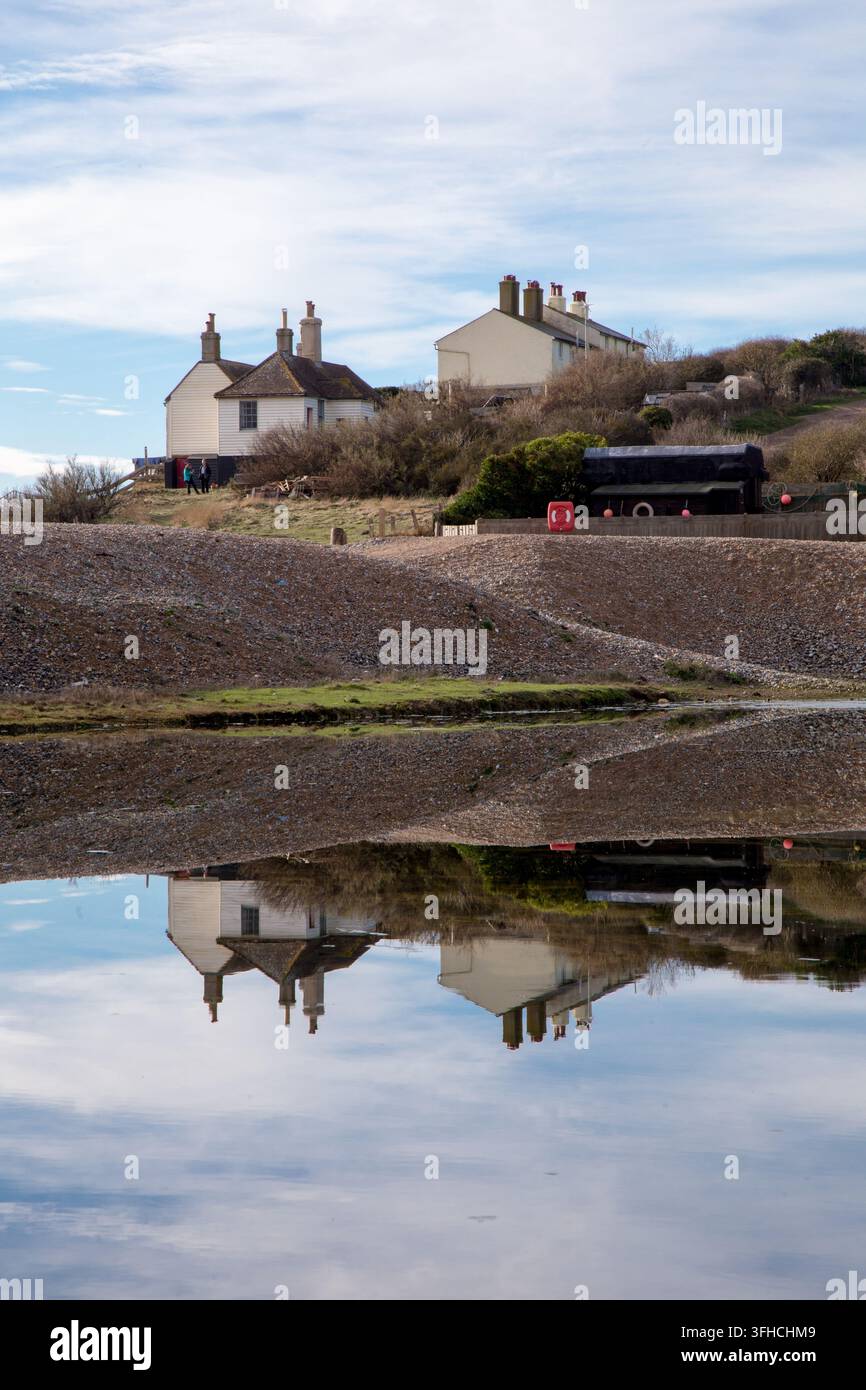 Cottages historiques des gardes-côtes parfaitement reflétés dans un plan d'eau calme derrière la plage de galets à Cuckmere Haven, East Sussex. Banque D'Images
