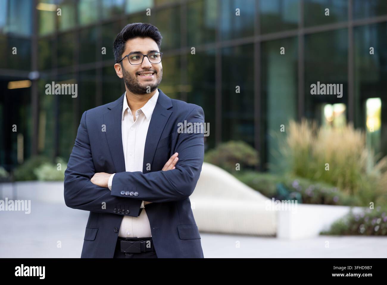 Jeune homme d'affaires indien confiant debout les bras croisés, portrait professionnel d'un entrepreneur prospère dans un parc de bureaux moderne. Carrière réussie et leadership. Banque D'Images