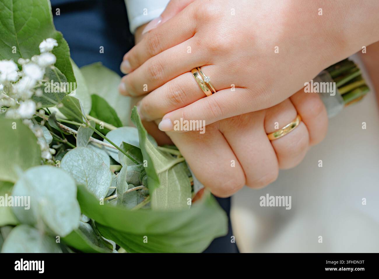 couple romantique se tenant la main avec des alliances en or et blanc devant des feuillages et des fleurs, gros plan vu d'en haut dans un cadre extérieur avec métal Banque D'Images