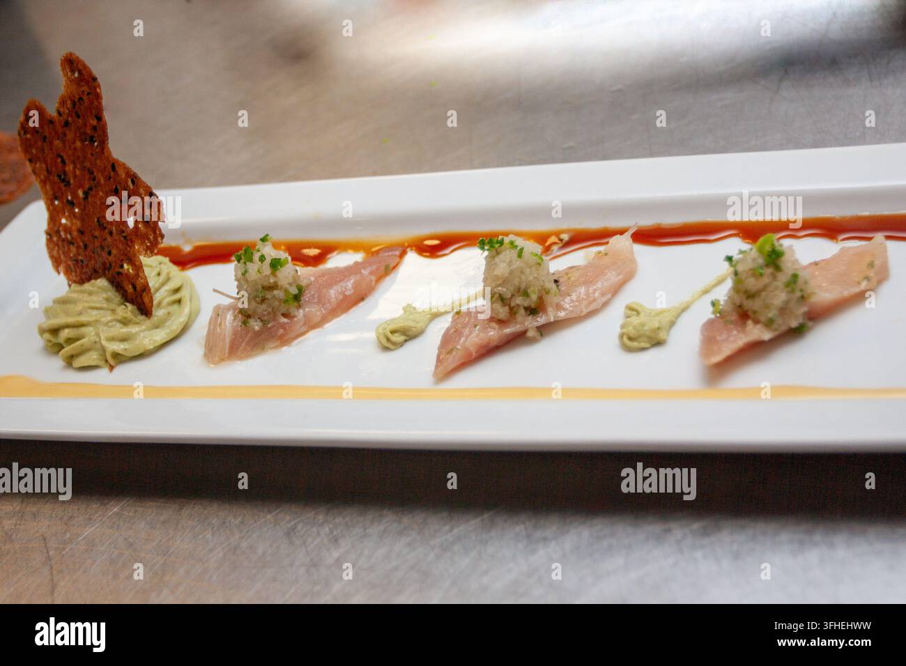 Une entrée de crudo de poisson finement arrangée sur une assiette rectangulaire allongée, mettant en vedette du poisson blanc cru finement tranché, recouvert d'un mi Banque D'Images
