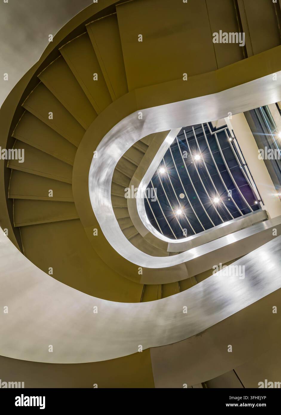 Des marches courbes et lisses montent en spirale autour d'une ouverture centrale, laissant la lumière vive s'infiltrer à travers la structure géométrique au-dessus. Banque D'Images