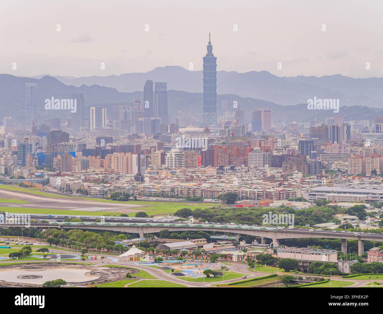 Taipei 101 s'élève au-dessus d'un paysage urbain dense de gratte-ciel et de zones résidentielles basses près d'une piste d'atterrissage d'aéroport. Banque D'Images