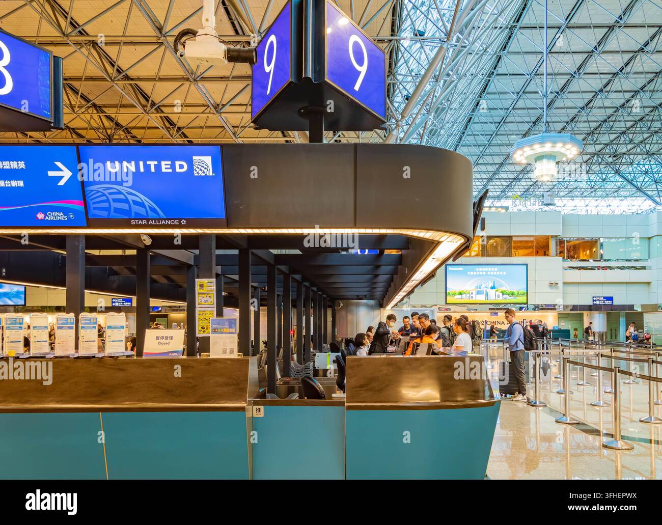 Les voyageurs font la queue à un comptoir d'enregistrement de United Airlines sous un grand panneau bleu indiquant le numéro de porte dans un terminal aéroportuaire spacieux. Banque D'Images
