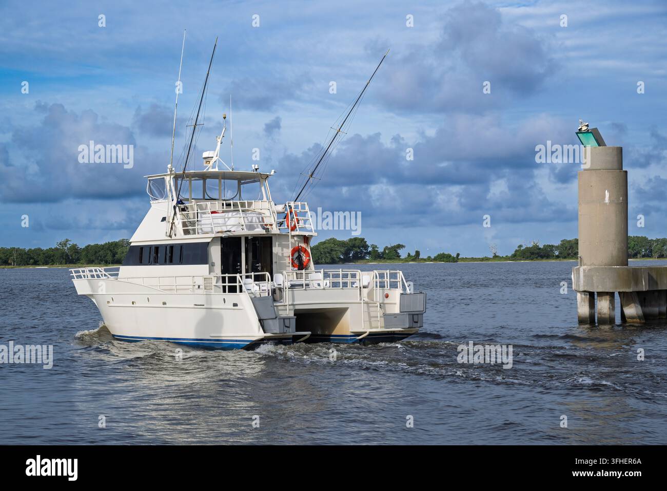 Un robuste bateau de pêche commerciale s'éloigne des quais de la marina de Biloxi, sa coque blanche creusant une vague douce à travers les eaux turquoise et calmes de Banque D'Images