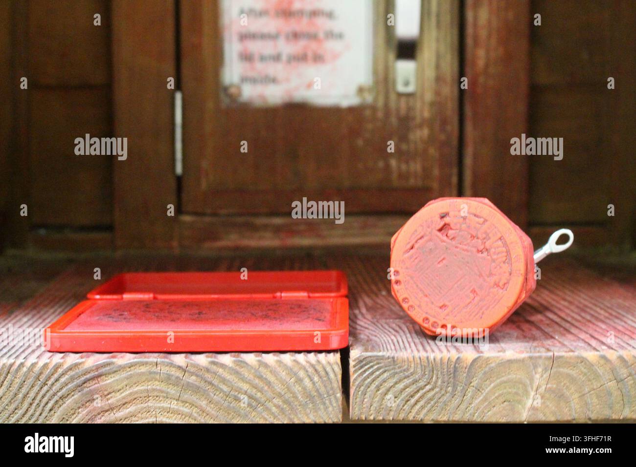 Une vue rapprochée montre un tampon encreur rouge ouvert à côté d'un tampon circulaire en bois posé sur un support en bois rustique à l'intérieur d'une boîte de station de tamponnage de pèlerinage le long du Banque D'Images