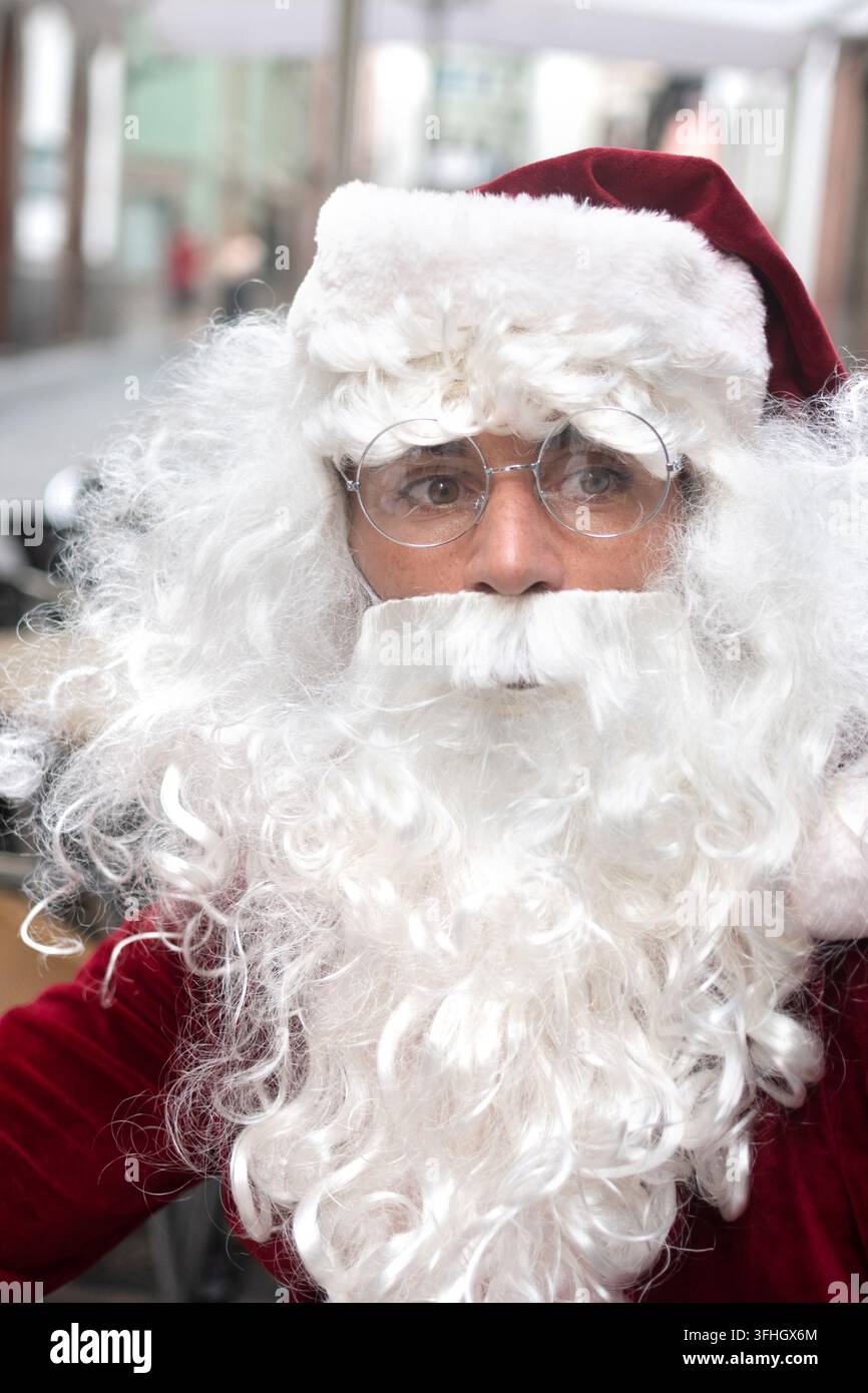 Portrait rapproché du Père Noël portant une tenue rouge traditionnelle, une barbe blanche et des lunettes rondes tout en regardant directement la caméra. Banque D'Images