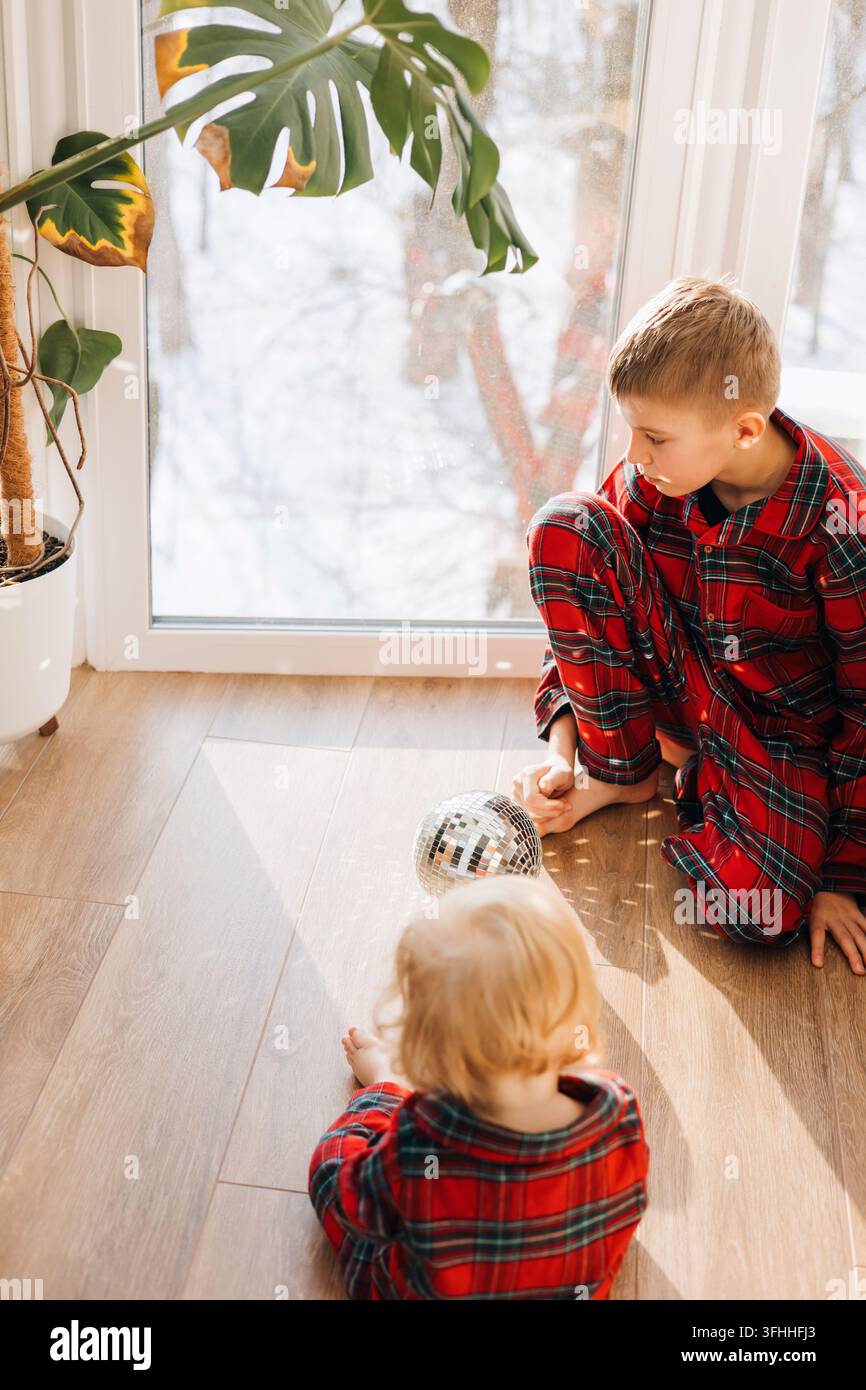 Deux frères en pyjamas à carreaux assortis jouant avec des décorations de Noël à la maison Banque D'Images