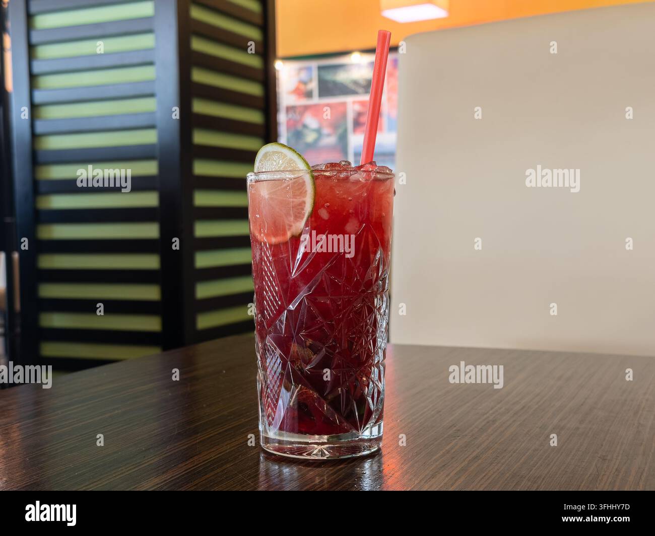 Boisson fruitée rouge glacée servie dans un gobelet en cristal décoratif avec une paille, capturant un moment de détente hydratant en été dans un restaurant moderne Banque D'Images