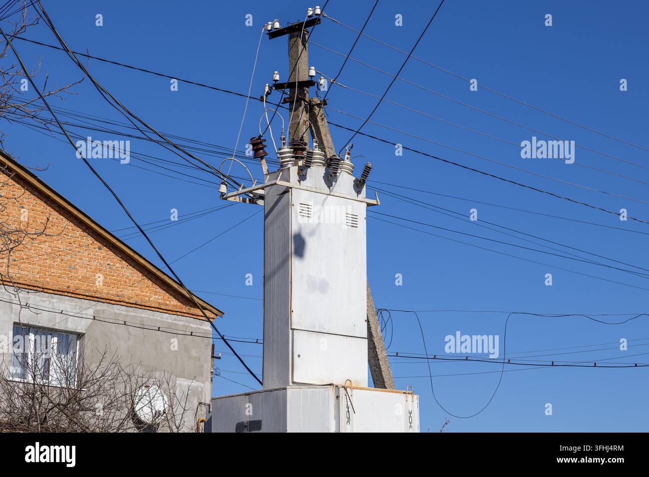 Un boîtier de transformateur industriel monté sur un poteau utilitaire érodé alimente les bâtiments voisins en électricité, reflétant la technologie de transmission d'énergie Banque D'Images