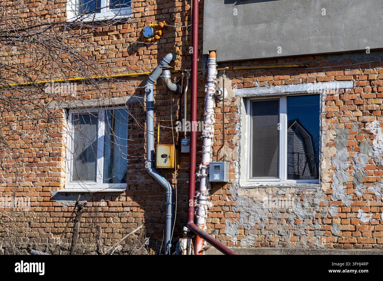 Un mur extérieur d'une maison résidentielle en brique présentant des conduits utilitaires exposés et des fenêtres en vinyle qui captent l'intersection de l'architecture traditionnelle Banque D'Images