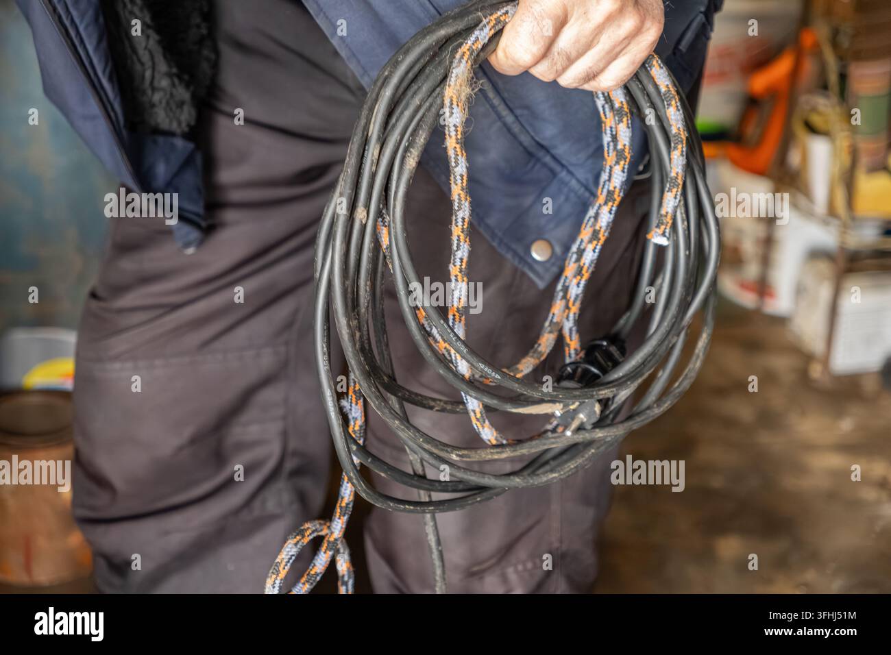 Un électricien porte un câble d'extension regroupé dans un atelier, évoquant des thèmes de rénovation, de travail physique, de rangement organisé, professionnel ha Banque D'Images