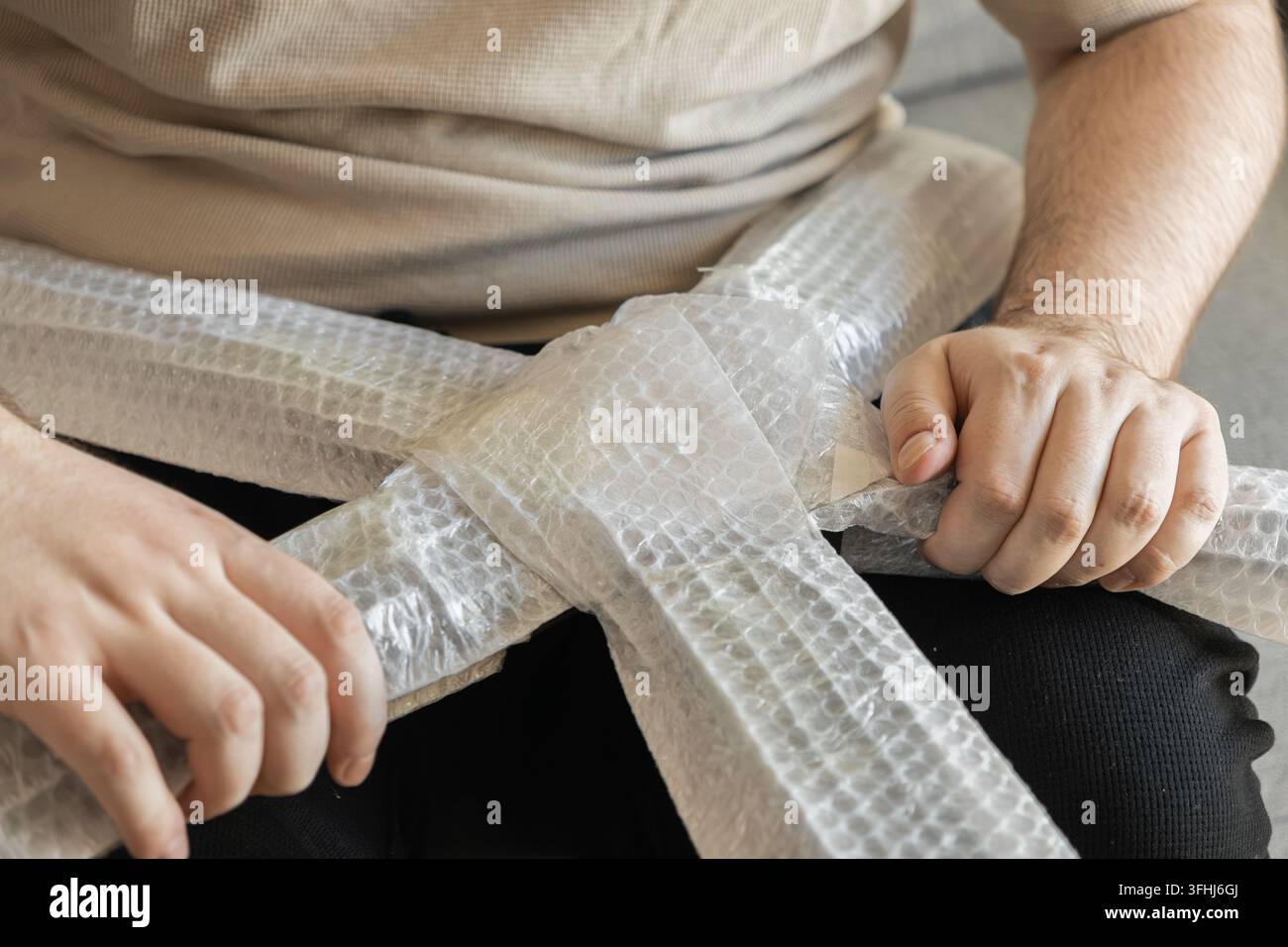 Une personne emballe soigneusement les pièces d'une chaise en bois avec du papier bulle en plastique, démontrant une préparation attentive pour un transport sécurisé lors d'un déménagement domestique Banque D'Images