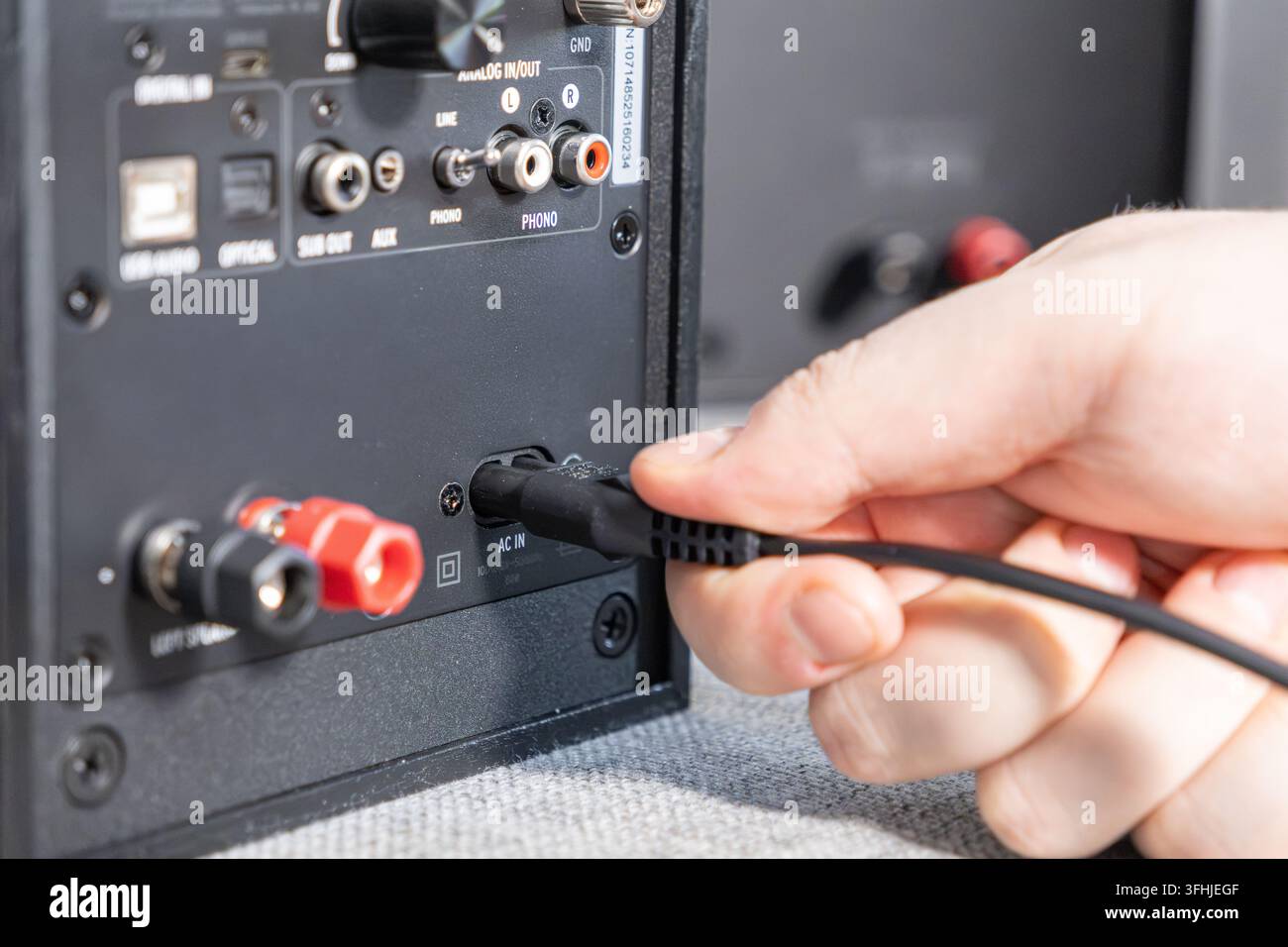 Close-up d'une personne connectant un câble électrique noir à l'arrière d'un haut-parleur alimenté, illustrant la configuration matérielle pour l'entertainment domestique Banque D'Images