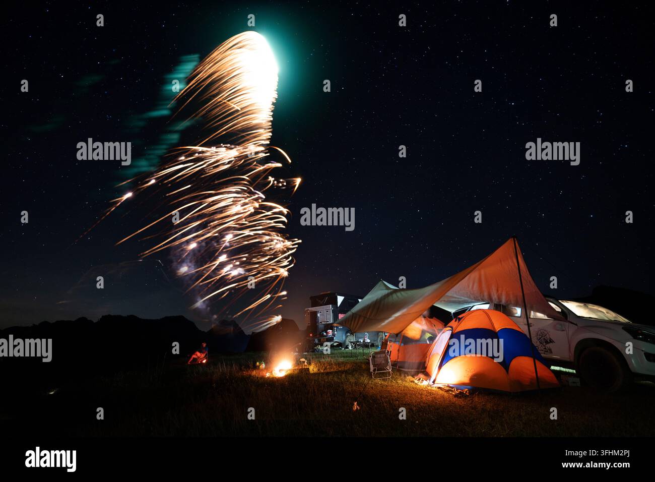 Les feux d'artifice en forme d'étoiles filantes strient au-dessus d'un camp nocturne illuminé, Suoi Bon, Moc Chau, Vietnam Banque D'Images