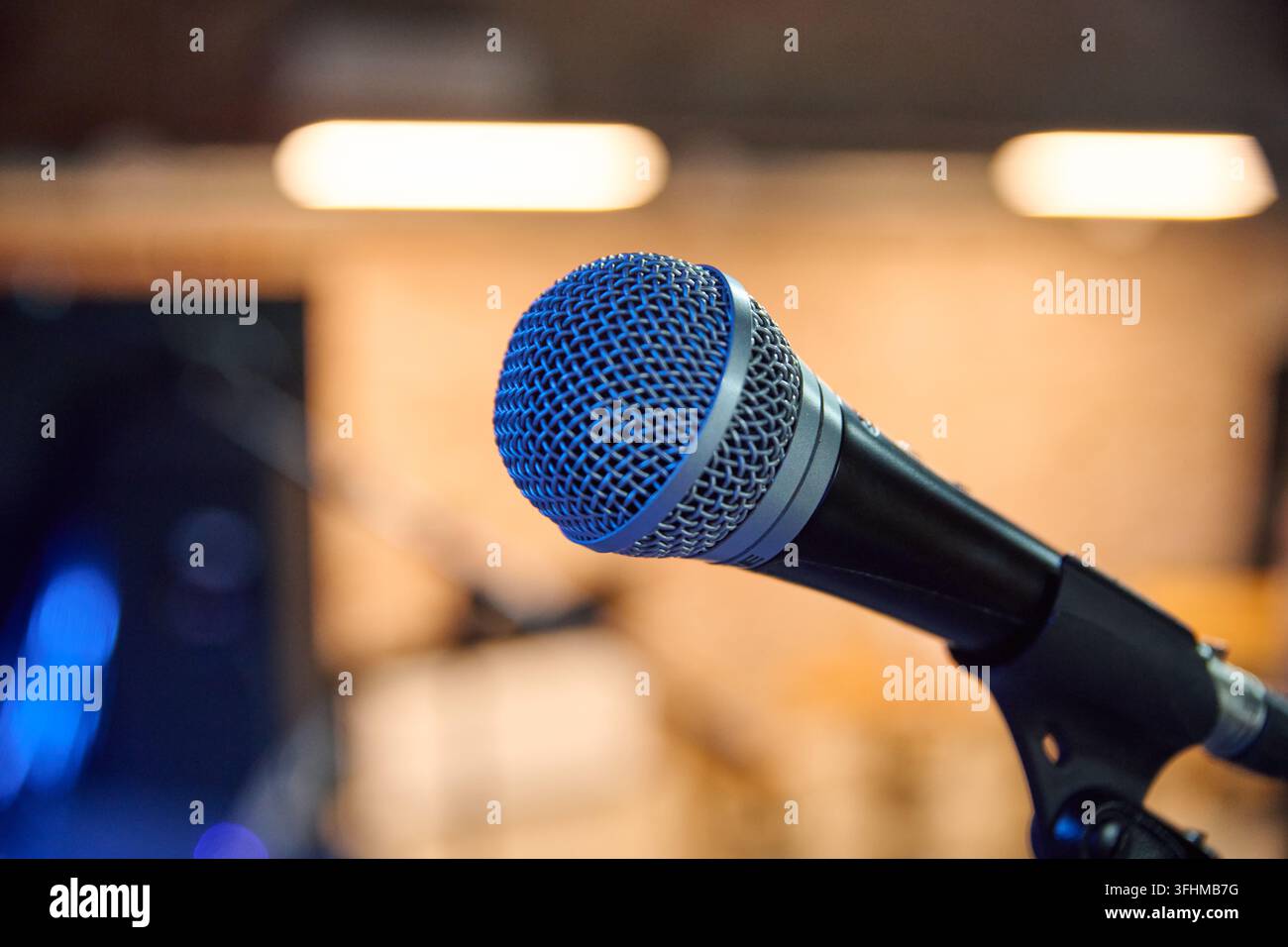 Micro en maille bleue s'étendant à travers un studio d'enregistrement chaleureux avec des lumières floues, un équipement sombre et une mise au point peu profonde, offrant une imagerie audio claire pour Broa Banque D'Images