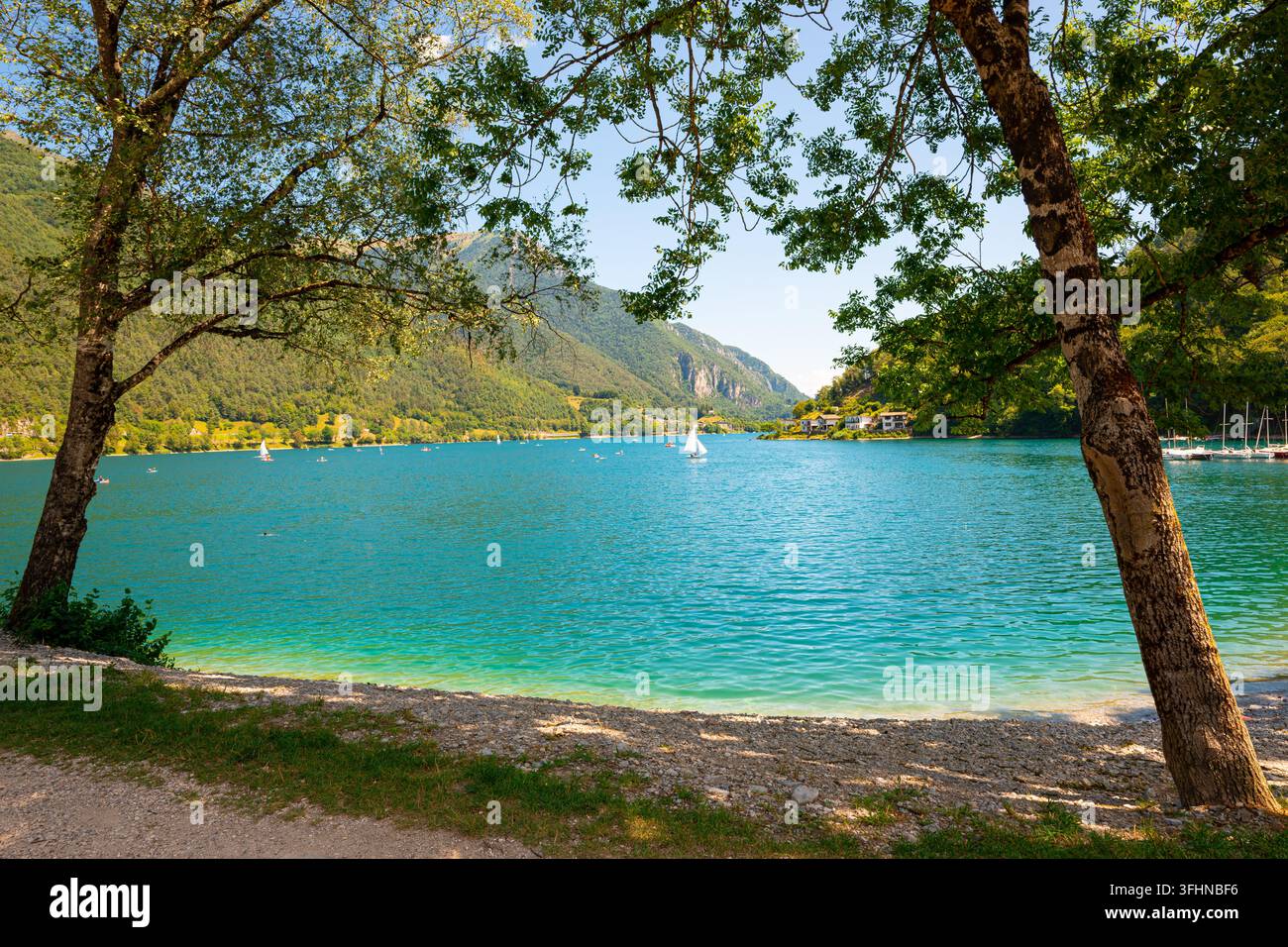 Lac turquoise Ledro dans le nord de l'Italie encadré par des arbres avec des voiliers et une rive sablonneuse par une journée d'été ensoleillée. Banque D'Images