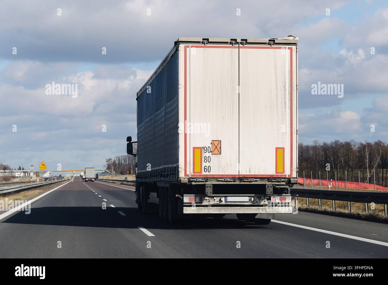 Camion de marchandises blanc roulant sur l'autoroute sous un ciel nuageux. Fond de transport pour la logistique de fret, la livraison routière et le trafic commercial. Banque D'Images