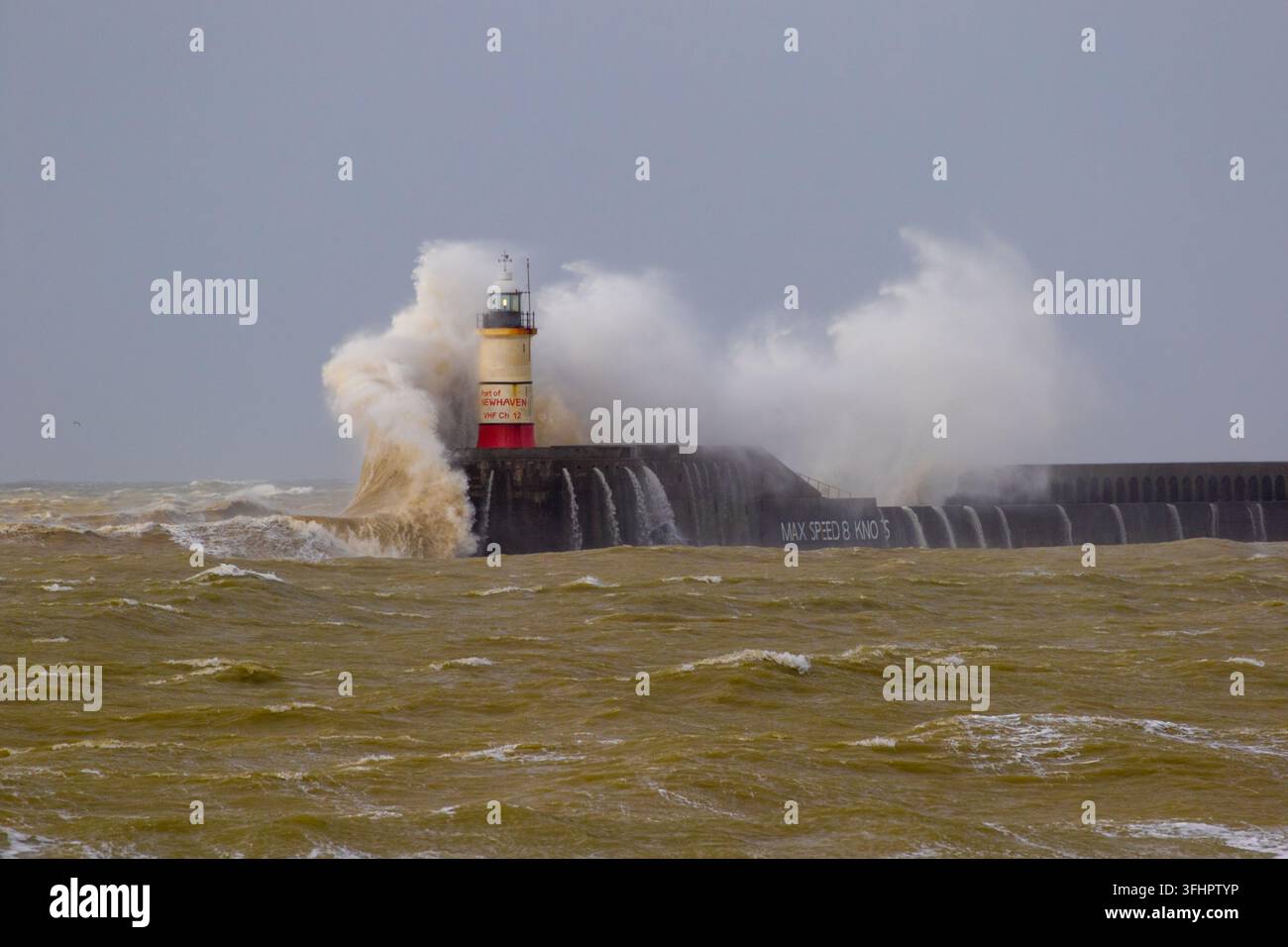 Une vague océanique massive et explosive s'écrase sur le phare historique de Newhaven et le mur de brise-lames lors d'une tempête hivernale violente. Banque D'Images