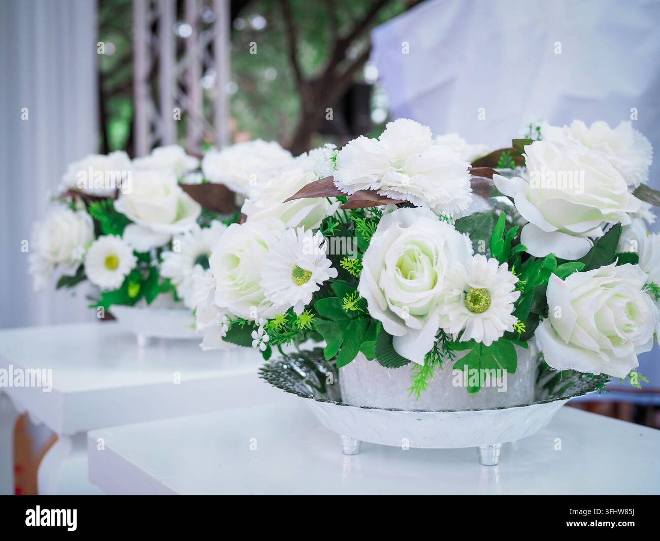 Centre de table blanc floral avec des roses et des feuilles vertes sur des tables blanches Banque D'Images