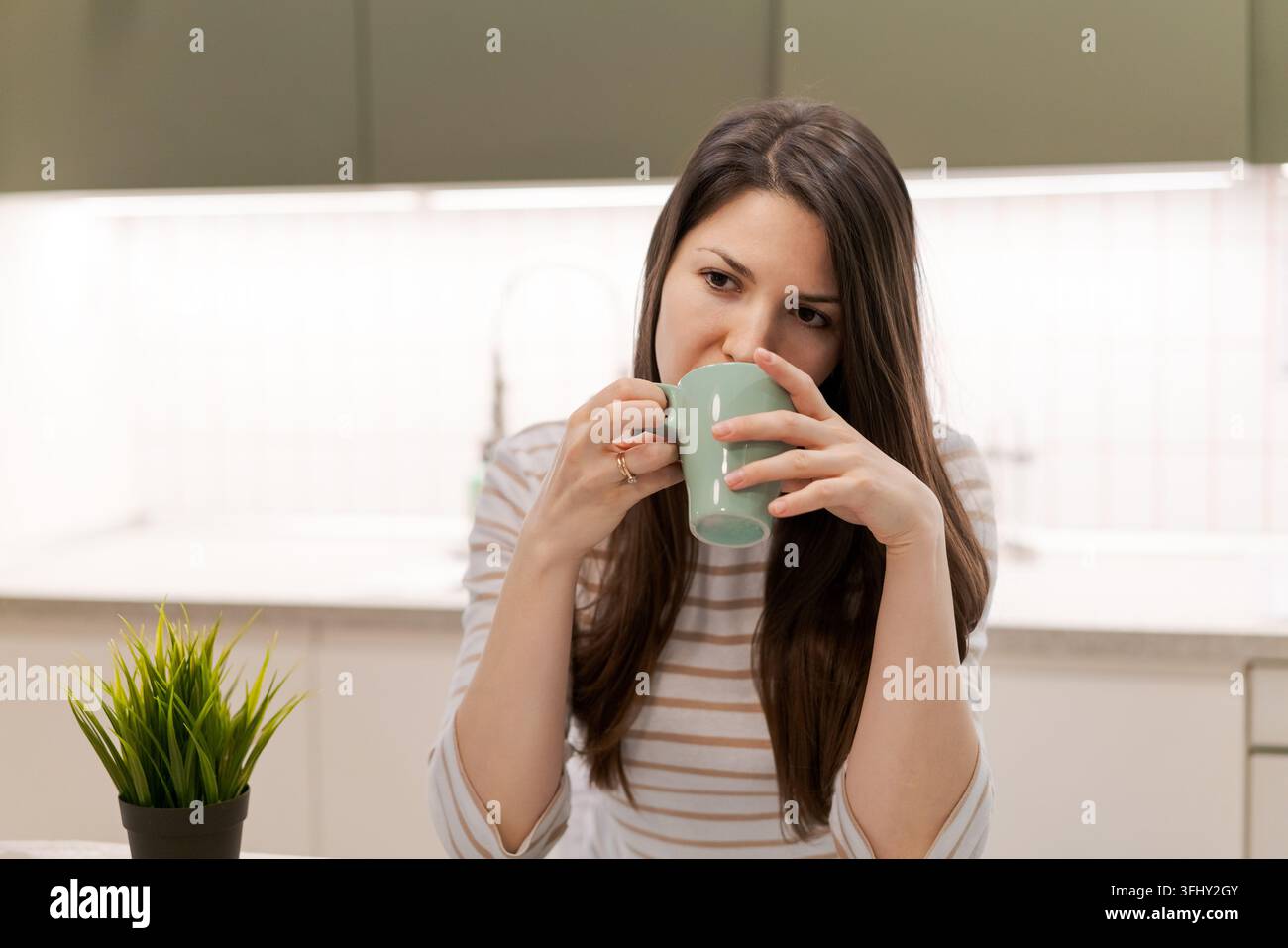Une femme boit du café dans une tasse verte Banque D'Images