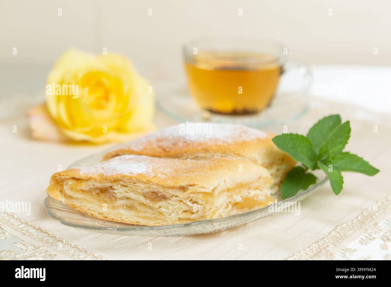 Il y a deux parts de tarte aux pommes, des myrtilles et des feuilles de menthe sur l'assiette, une tasse de thé à côté, et la table est décorée d'une rose vivante. Banque D'Images