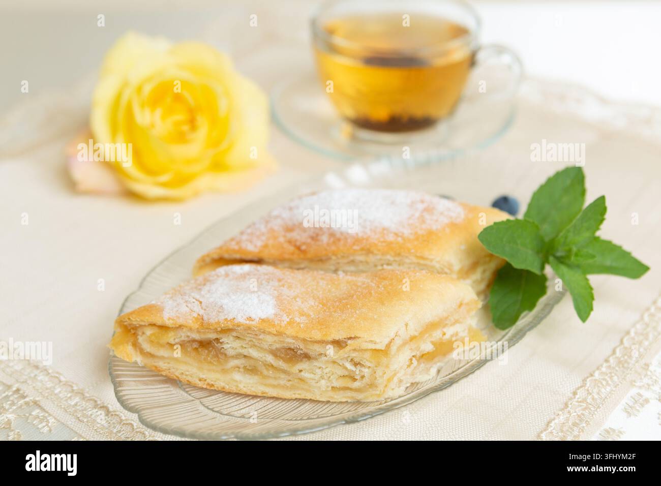 Il y a deux parts de tarte aux pommes, des myrtilles et des feuilles de menthe sur l'assiette, une tasse de thé à côté, et la table est décorée d'une rose vivante Banque D'Images