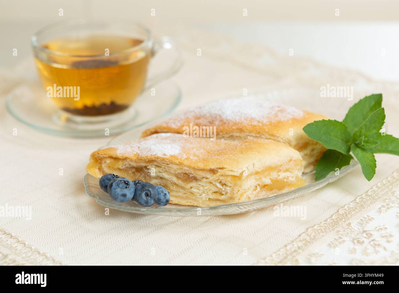 Il y a deux parts de tarte aux pommes, des myrtilles et des feuilles de menthe sur l'assiette, une tasse de thé à côté Banque D'Images