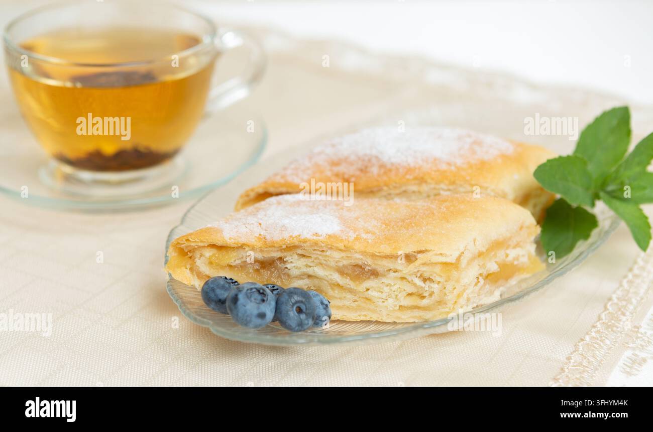 Il y a deux parts de tarte aux pommes, des myrtilles et des feuilles de menthe sur l'assiette, une tasse de thé à côté Banque D'Images