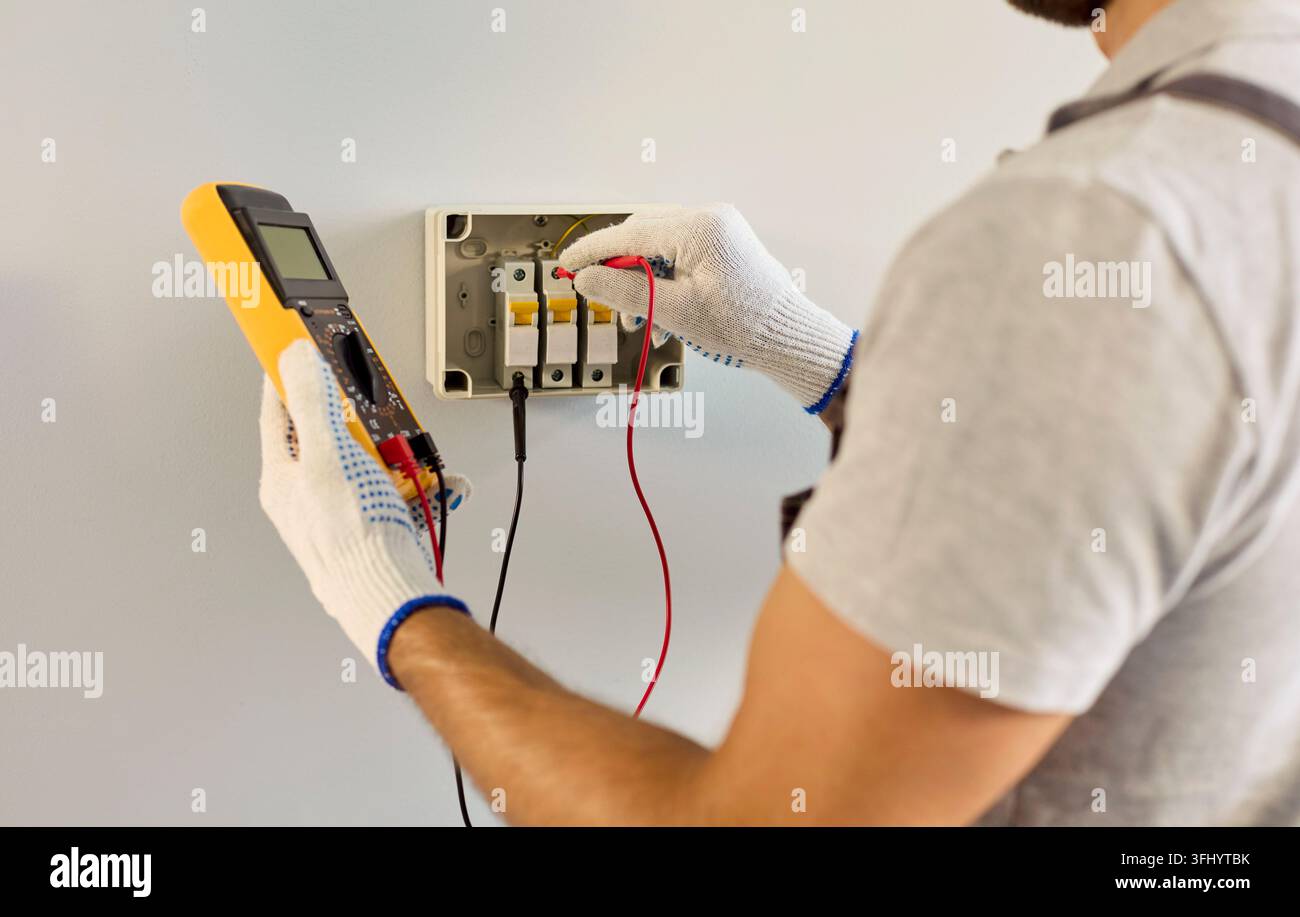 Gros plan d'un électricien testant un tableau de disjoncteurs avec un multimètre à l'intérieur Banque D'Images