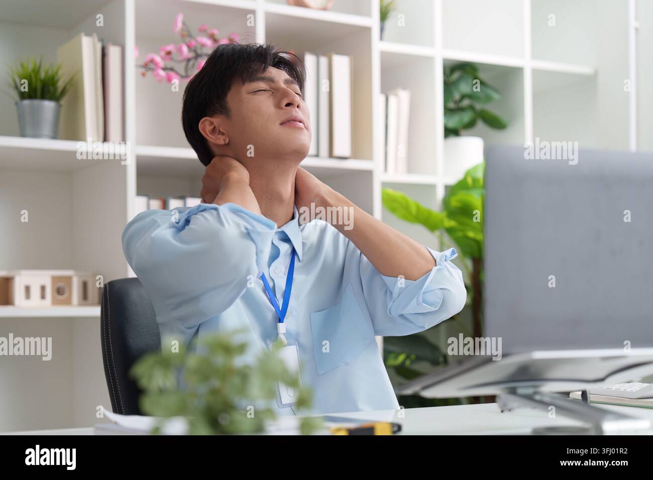 Homme asiatique souffrant de douleurs au cou et à l'épaule tout en travaillant au bureau Banque D'Images