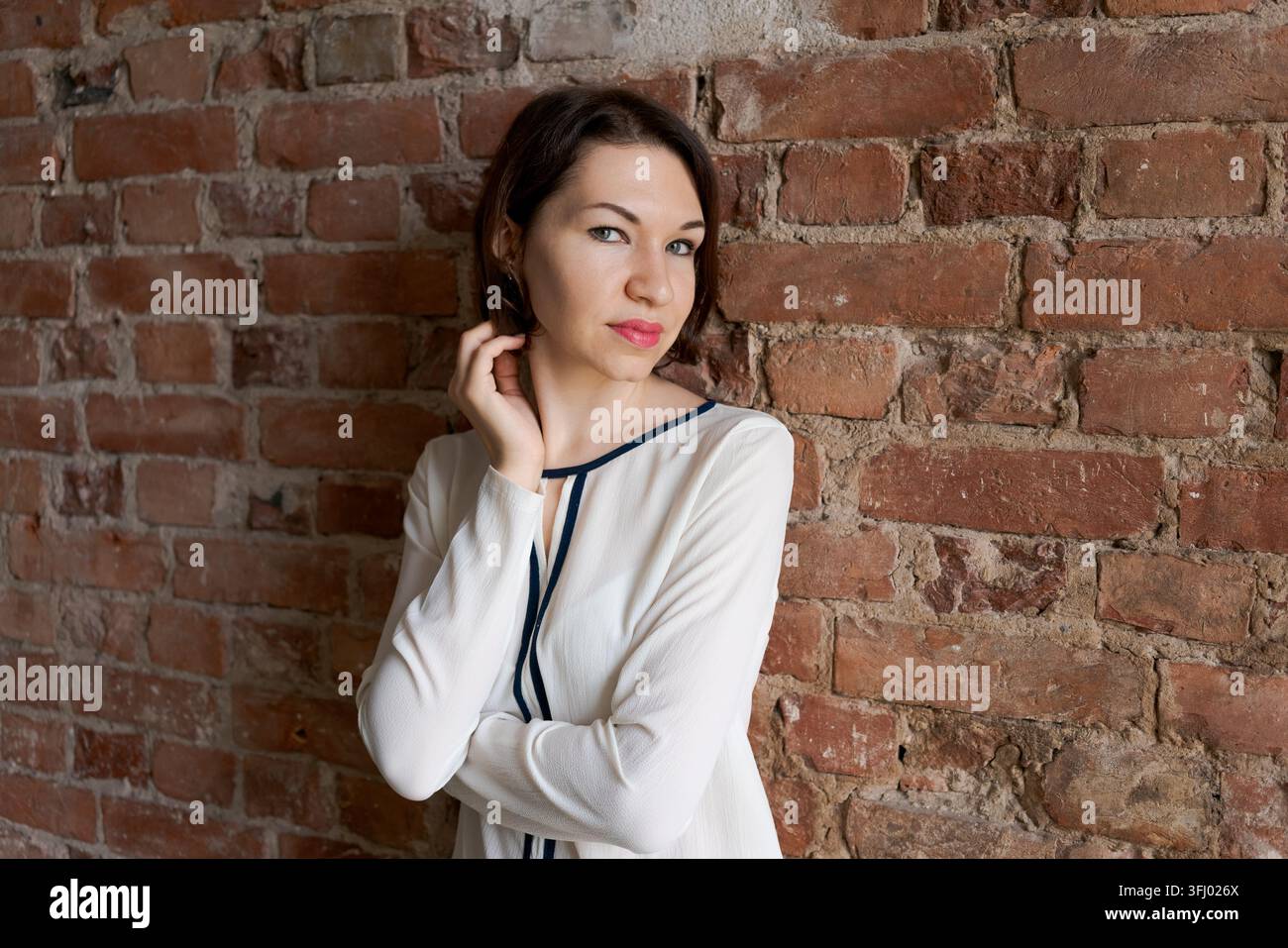 Femme brune confiante avec un regard direct devant un mur de briques apparentes rustique dans un studio loft Banque D'Images