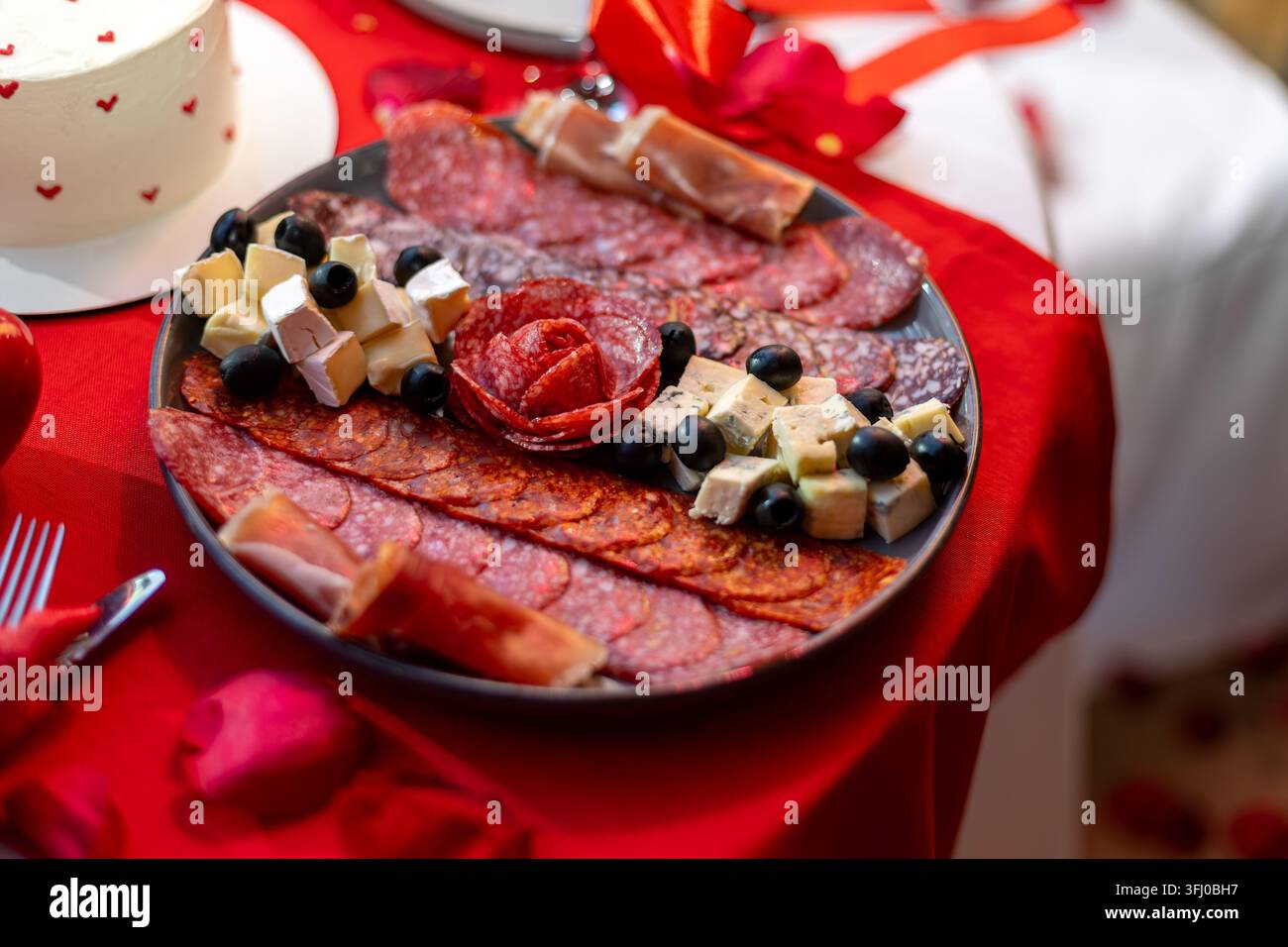 Plateau de charcuterie avec fromage, olives et viandes séchées. Plateau de charcuterie avec divers viandes séchées, fromages et olives noires sur un rouge romantique Banque D'Images