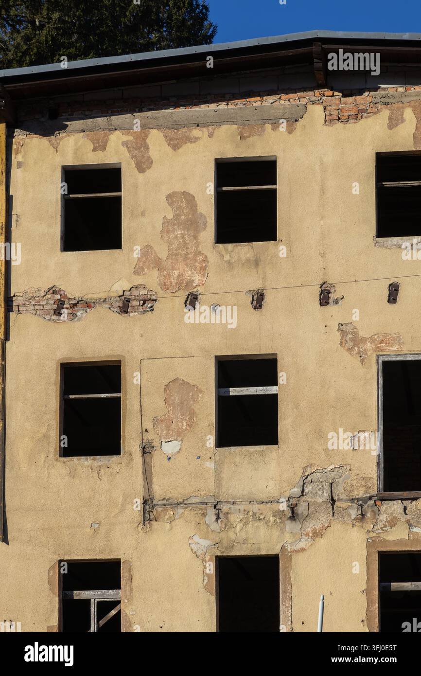 Un mur extérieur vieilli mettant en évidence un plâtre écaillé et une maçonnerie apparente d'une structure délabrée, capturant une ambiance sombre de transition historique Banque D'Images