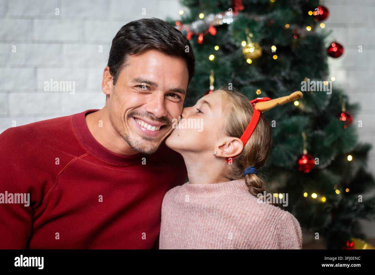 Fille embrassant son père souriant pendant la célébration de Noël à la maison Banque D'Images